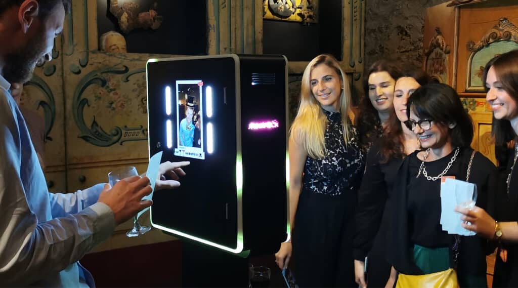 Borne photo shootnbox double face lors d'un évènement. Un homme se prend en photo d'un côté et de l'autre 5 femmes posent devant l'objectif en souriant