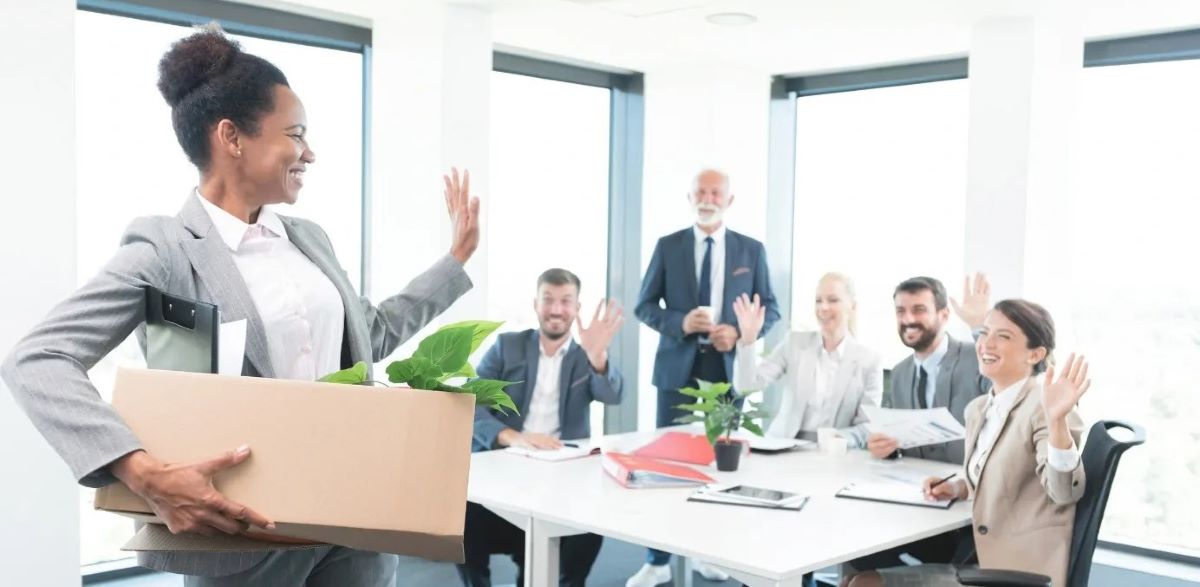 employée femme afro carton sous le bras avec affaire dit au revoir à ses collègue autour d'une table réunion
