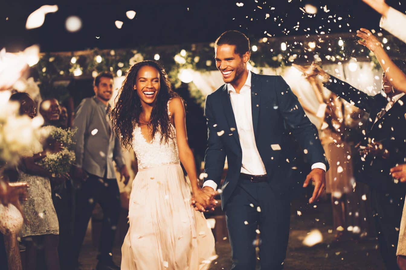 Jeunes mariés entrant dans la salle de réception sous les applaudissements et les confettis, entourés d'invités heureux formant une haie d'honneur couple mixte