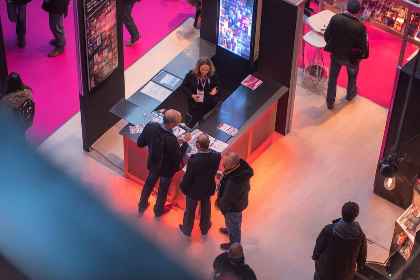 Vue du dessus d’un stand salon professionnel avec visiteurs en interaction chez le commerçant et ambiance dynamique